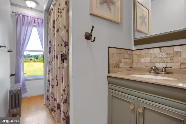 bathroom featuring decorative backsplash, hardwood / wood-style floors, vanity, and radiator heating unit