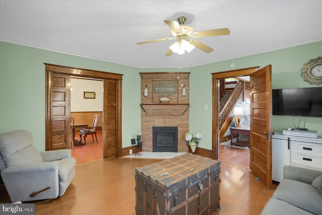 living room featuring hardwood / wood-style flooring, ceiling fan, ornamental molding, brick wall, and a brick fireplace