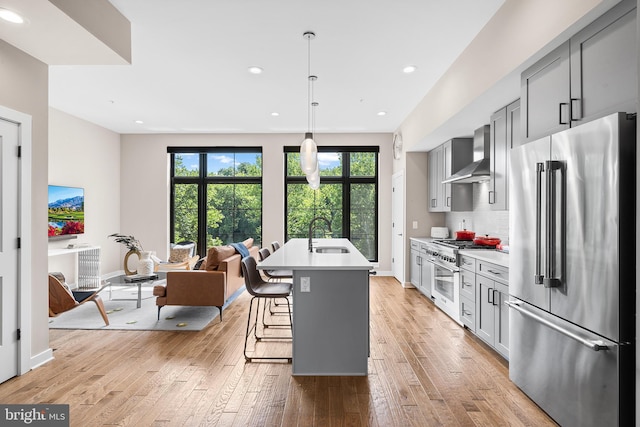 kitchen with high quality appliances, a kitchen island with sink, a kitchen breakfast bar, wall chimney exhaust hood, and gray cabinets