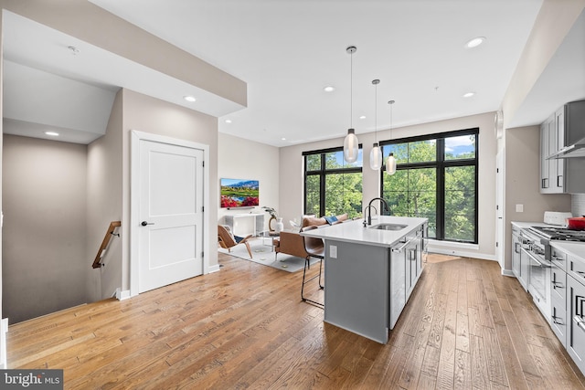 kitchen with pendant lighting, a breakfast bar, a kitchen island with sink, sink, and light hardwood / wood-style floors