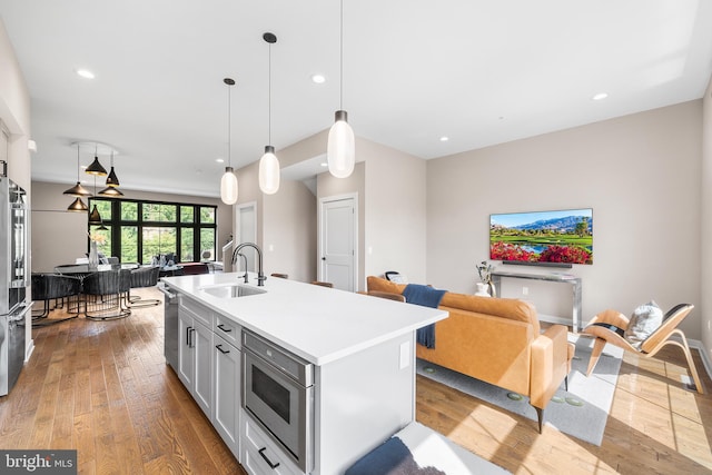 kitchen featuring sink, stainless steel appliances, light hardwood / wood-style flooring, decorative light fixtures, and a kitchen island with sink