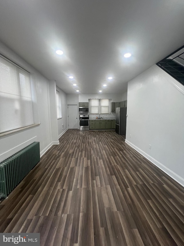 basement with dark wood-type flooring, stainless steel fridge, and radiator heating unit