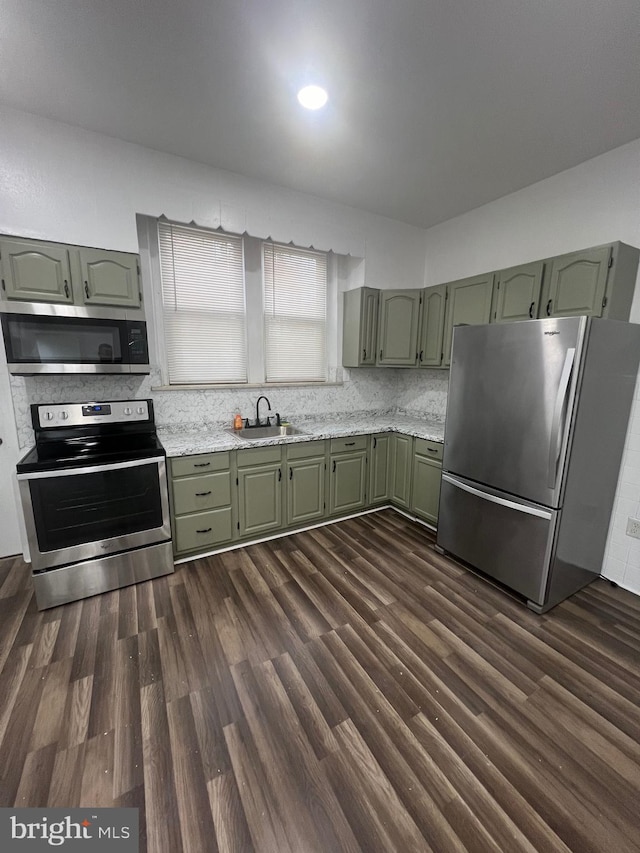 kitchen featuring dark wood-type flooring, green cabinets, appliances with stainless steel finishes, decorative backsplash, and sink