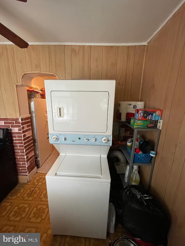 laundry room featuring crown molding, stacked washer / drying machine, and wood walls