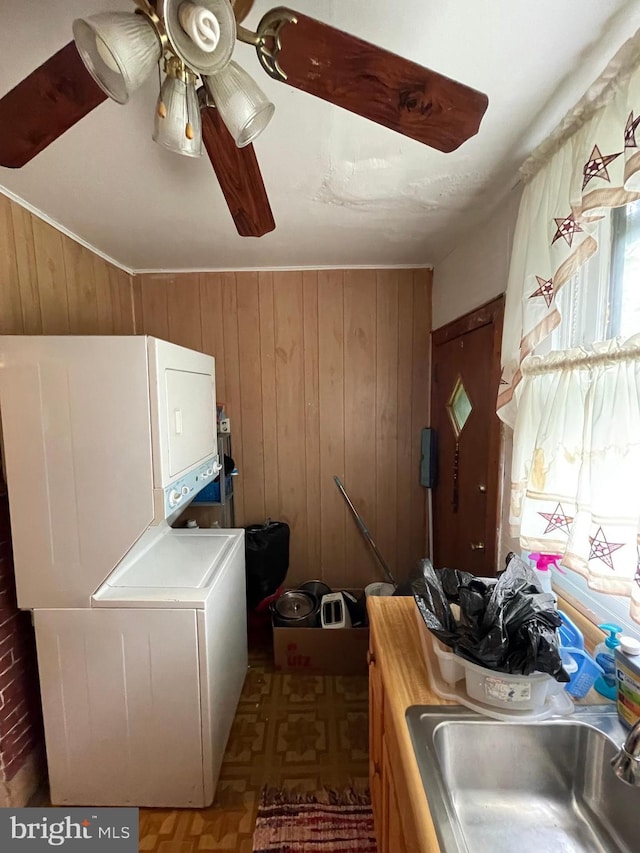 washroom featuring ceiling fan, stacked washing maching and dryer, sink, and wooden walls