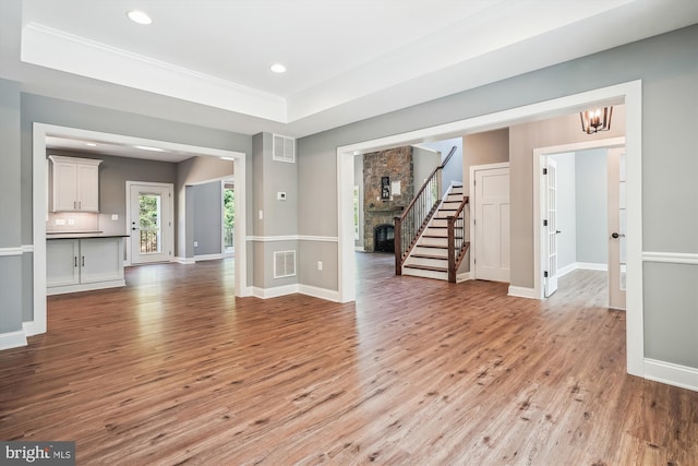 unfurnished living room featuring a notable chandelier, a stone fireplace, a raised ceiling, and light hardwood / wood-style flooring