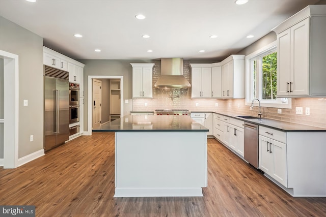 kitchen featuring sink, wall chimney exhaust hood, a kitchen island, white cabinets, and appliances with stainless steel finishes