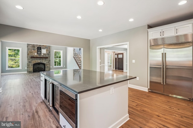 kitchen featuring a center island, built in appliances, light wood-type flooring, a fireplace, and white cabinetry