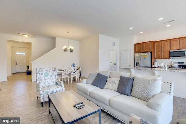 living room featuring light hardwood / wood-style floors, sink, washer / clothes dryer, and a chandelier