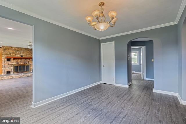 empty room with hardwood / wood-style floors, ceiling fan with notable chandelier, a stone fireplace, and ornamental molding