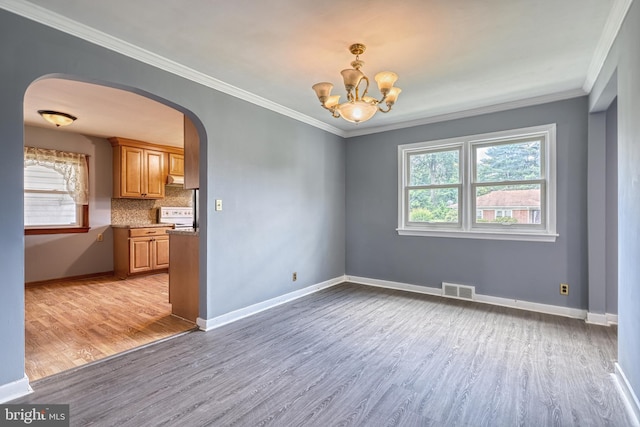 empty room with a notable chandelier, ornamental molding, and light hardwood / wood-style flooring