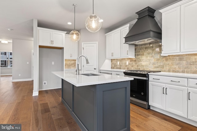 kitchen with stainless steel gas range oven, custom range hood, sink, a center island with sink, and white cabinetry