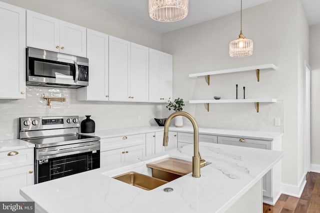 kitchen featuring light stone counters, sink, stainless steel appliances, and decorative light fixtures