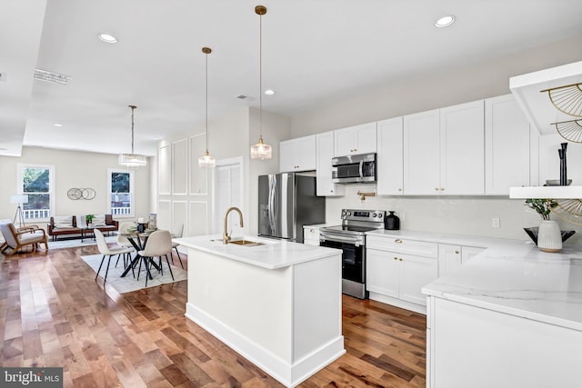 kitchen featuring white cabinets, stainless steel appliances, hanging light fixtures, and an island with sink