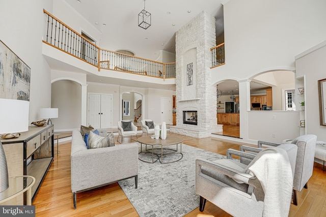 living room with light wood-type flooring, a towering ceiling, a stone fireplace, and ornate columns