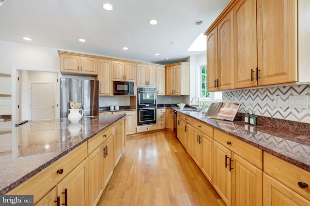 kitchen with black appliances, sink, light hardwood / wood-style flooring, light brown cabinetry, and dark stone counters