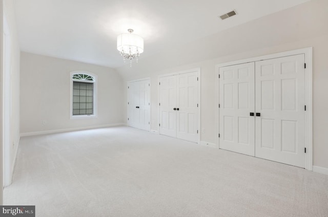 unfurnished bedroom featuring light carpet, multiple closets, a chandelier, and lofted ceiling