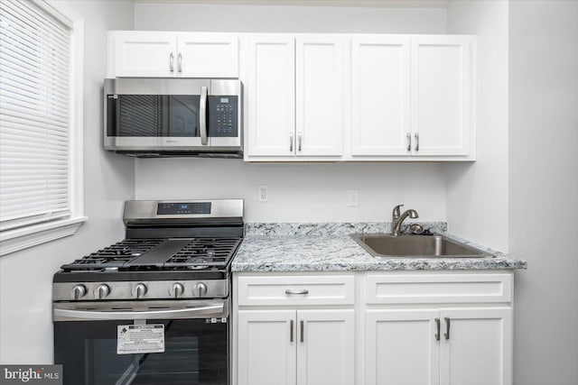 kitchen with light stone counters, stainless steel appliances, white cabinetry, and sink