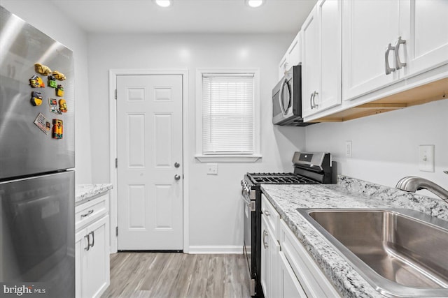 kitchen featuring white cabinets, sink, light wood-type flooring, appliances with stainless steel finishes, and light stone counters