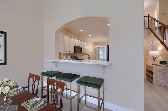 kitchen with a breakfast bar, white cabinets, hanging light fixtures, range with electric stovetop, and kitchen peninsula