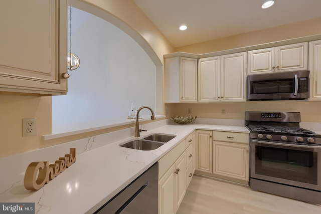 kitchen featuring light stone counters, sink, stainless steel appliances, and cream cabinetry