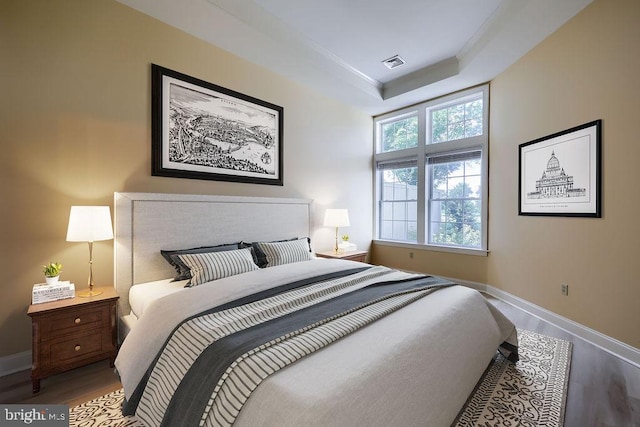 bedroom with hardwood / wood-style floors and a tray ceiling