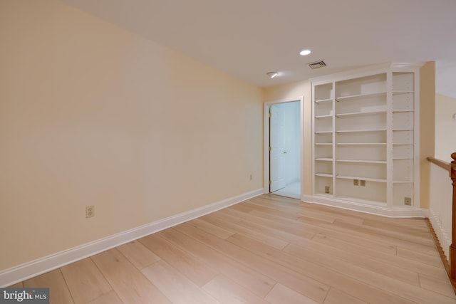 unfurnished room featuring built in shelves and light hardwood / wood-style floors