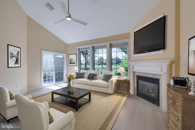 living room featuring light hardwood / wood-style floors, high vaulted ceiling, ceiling fan, and a tiled fireplace