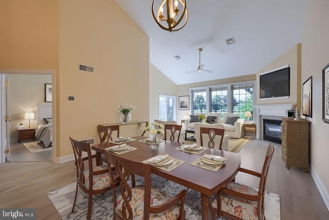 dining space featuring light hardwood / wood-style flooring, high vaulted ceiling, and ceiling fan with notable chandelier