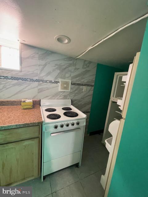 kitchen featuring electric range, light tile patterned flooring, and tile walls