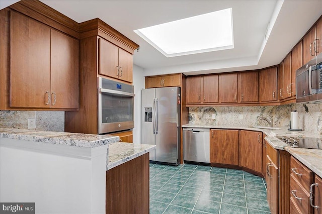 kitchen featuring sink, backsplash, appliances with stainless steel finishes, and a skylight