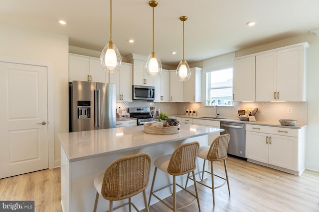 kitchen featuring decorative light fixtures, a kitchen island, white cabinetry, and appliances with stainless steel finishes