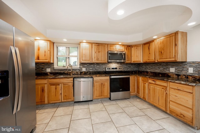 kitchen with appliances with stainless steel finishes, light tile patterned floors, dark stone counters, and sink