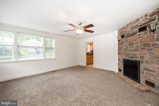 unfurnished living room featuring carpet flooring, a stone fireplace, and ceiling fan