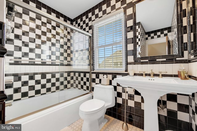 bathroom with bath / shower combo with glass door, tile walls, tile patterned flooring, and toilet