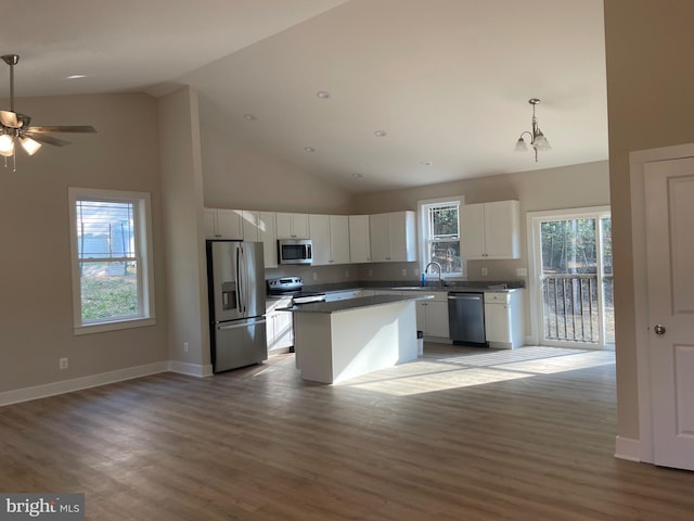 kitchen with high vaulted ceiling, hardwood / wood-style floors, a center island, white cabinetry, and appliances with stainless steel finishes