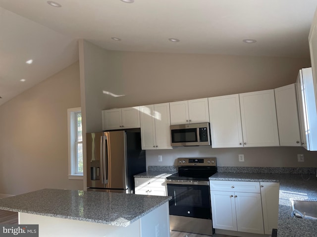 kitchen with white cabinets, a kitchen island, stone counters, high vaulted ceiling, and appliances with stainless steel finishes