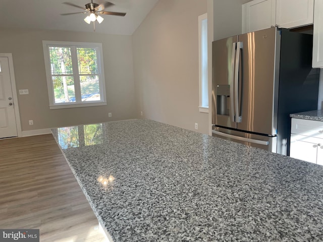 kitchen with wood-type flooring, lofted ceiling, light stone countertops, stainless steel refrigerator with ice dispenser, and white cabinetry