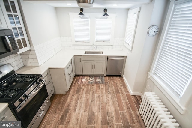 kitchen featuring hardwood / wood-style flooring, decorative backsplash, gray cabinetry, sink, and stainless steel appliances