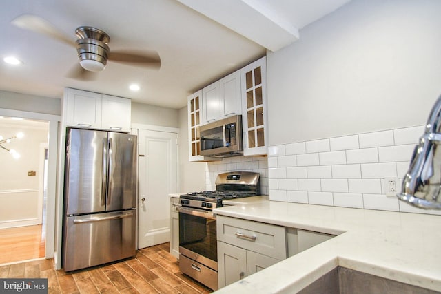 kitchen with appliances with stainless steel finishes, light hardwood / wood-style flooring, decorative backsplash, white cabinets, and ceiling fan