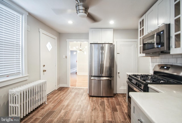 kitchen featuring stainless steel appliances, decorative backsplash, radiator, white cabinets, and wood-type flooring