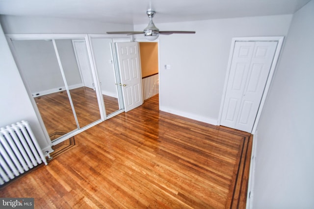 unfurnished bedroom featuring ceiling fan, hardwood / wood-style flooring, and radiator heating unit