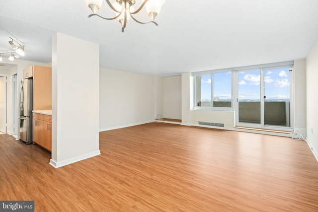 unfurnished living room featuring light wood-type flooring, a textured ceiling, and an inviting chandelier