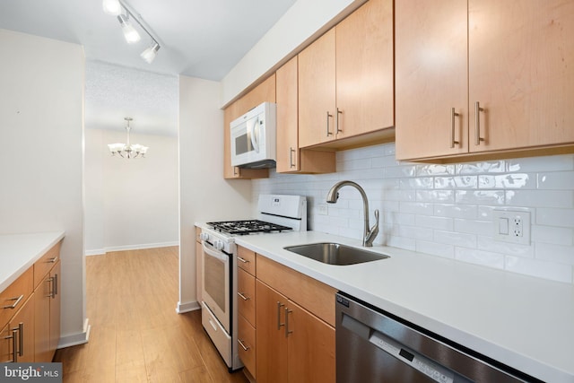 kitchen with appliances with stainless steel finishes, backsplash, sink, an inviting chandelier, and hanging light fixtures