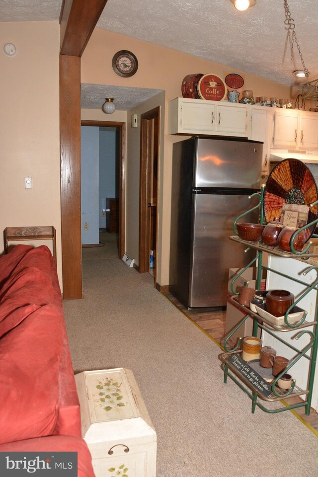 kitchen featuring lofted ceiling, light carpet, white cabinets, stainless steel fridge, and a textured ceiling