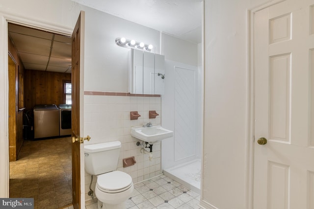 bathroom featuring toilet, tile patterned flooring, tile walls, and washing machine and clothes dryer