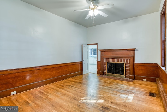 unfurnished living room featuring ceiling fan, light wood-type flooring, and a brick fireplace