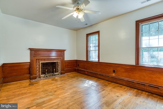 unfurnished living room featuring light hardwood / wood-style flooring, baseboard heating, a fireplace, and ceiling fan