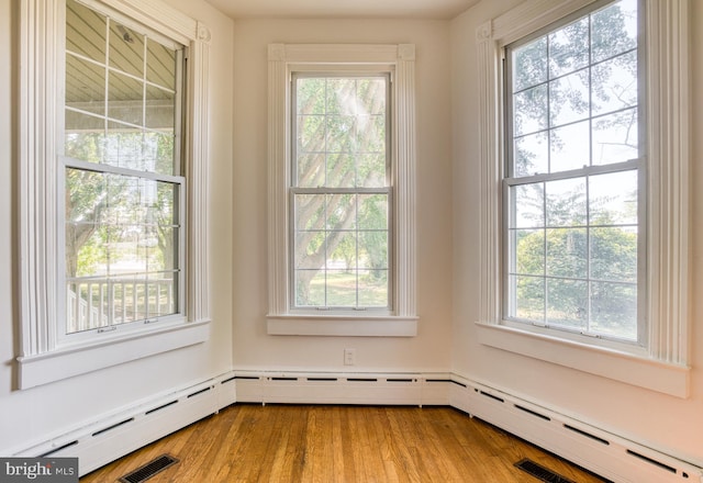 empty room featuring a baseboard heating unit, a healthy amount of sunlight, and hardwood / wood-style flooring