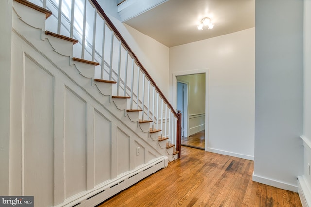 staircase with a baseboard heating unit and light hardwood / wood-style flooring